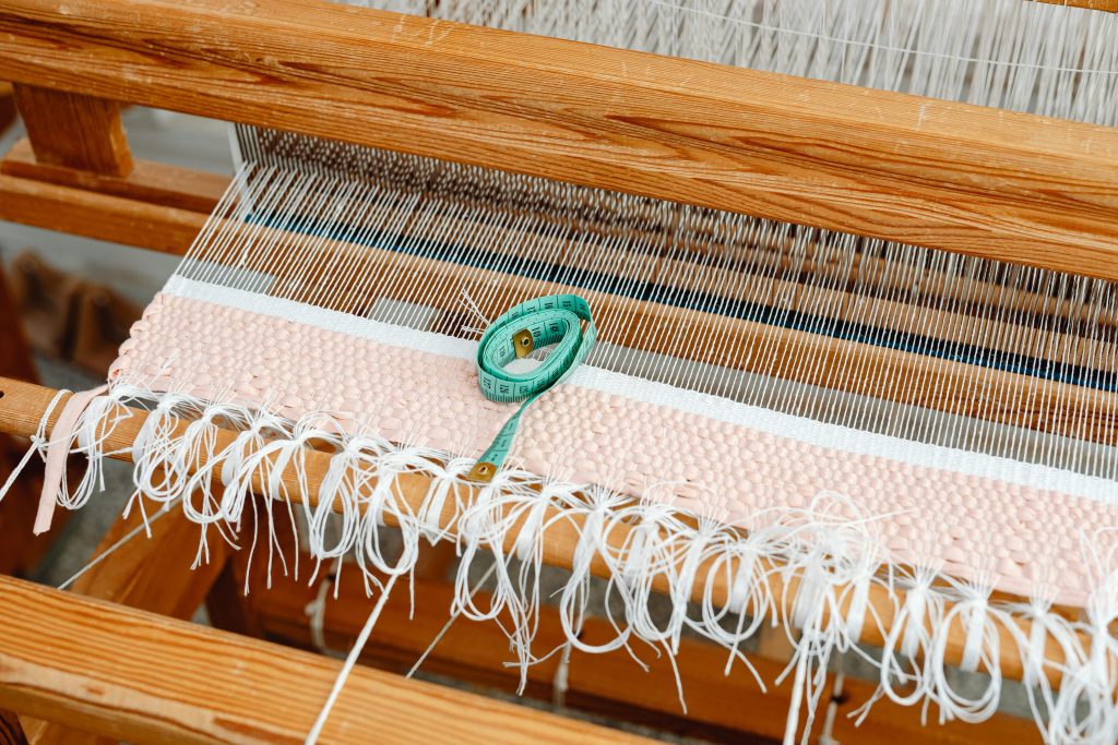 Detailed view of a wooden loom with woven fabric and a measuring tape, highlighting traditional weaving.