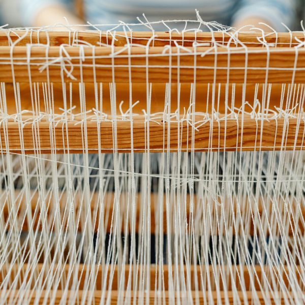 Detailed close-up of a wooden loom with white threads, showcasing traditional weaving.