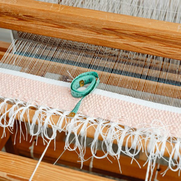 Detailed view of a wooden loom with woven fabric and a measuring tape, highlighting traditional weaving.
